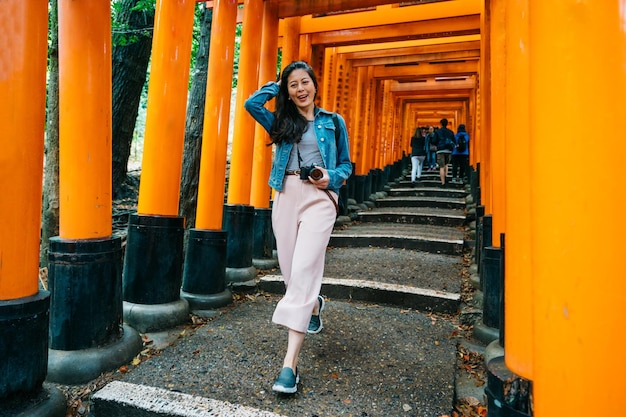 Full length photo of an elegant asian traveler walking in the torii and flicks her beautiful long hair. young lady fun on travel smiling and laughing during vacation trip in asia