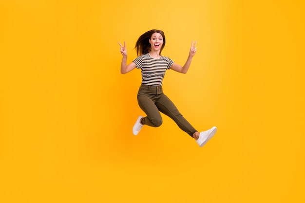 Full length photo of funky youth girl rest relax spring free time jump make v-sign wear stylish clothes isolated over bright color wall