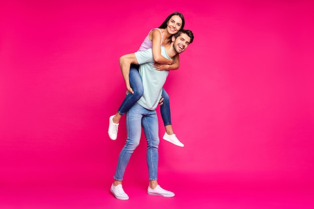 Full length photo of funny guy and lady holding piggyback spending best free time wear casual clothes isolated vibrant vivid pink color background