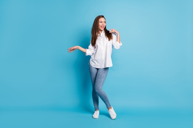 Full length photo of funny lady good mood dancing look side wear white shirt jeans sneakers isolated blue color background