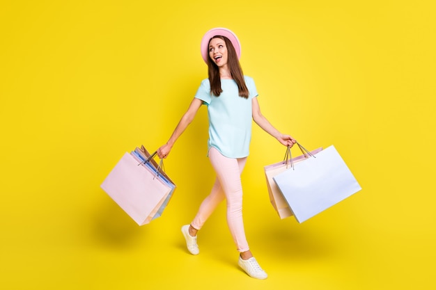 full length photo of girl tourist go walk mall impressed season rest relax sales hold many bags wear blue t-shirt pink pants trousers sunhat isolated over bright shine color background