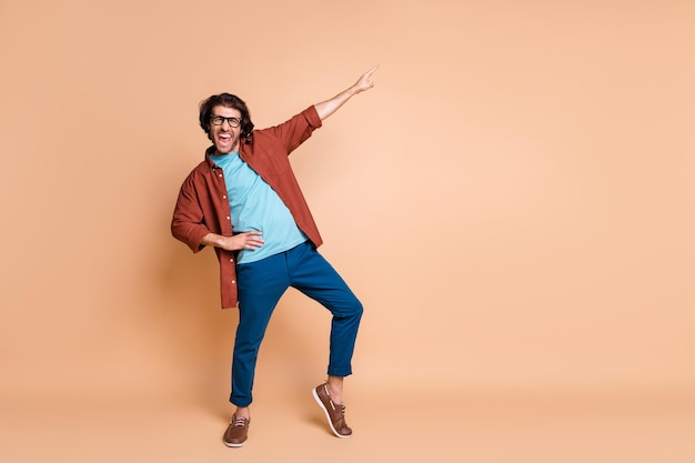 Full length photo of guy indicate finger up open mouth wear specs brown t-shirt pants shoes isolated beige color background