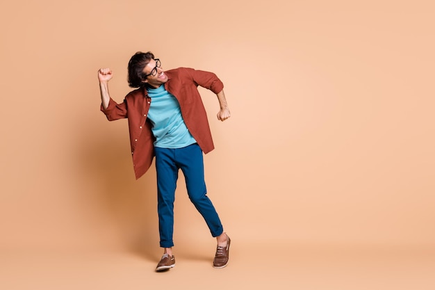 Full length photo of man dance open mouth wear specs brown t-shirt pants shoes isolated beige color background