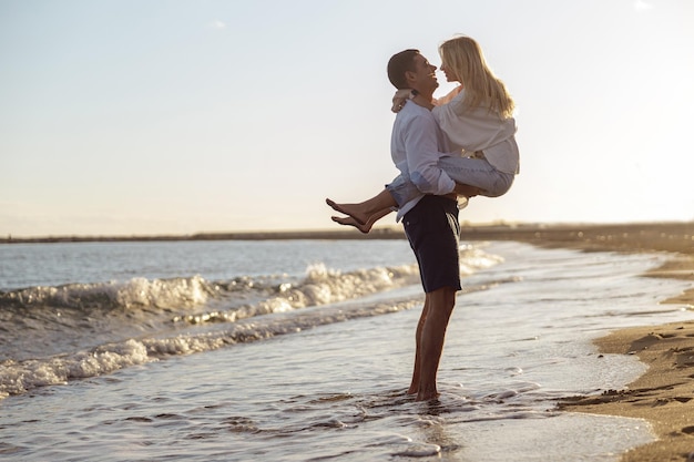 Photo full length photo of man holding woman in his arms standing by the sea