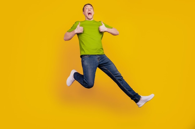 Full length photo of nice attractive cheerful optimistic guy show thum-up like cool jump up isolated over yellow background