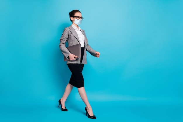 Full length photo of nice content smart lady specialist carrying laptop walking wear mask isolated over bright blue color background