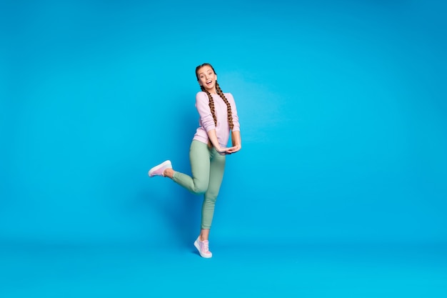 Полная фотография позитивной жизнерадостной девушки-подростка, у которой есть свободное время на прогулке со своими друзьями, чувствует себя удовлетворенной, носите современные розовые кроссовки, изолированные на синем цветном фоне