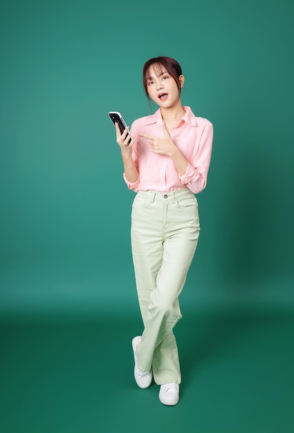 Full length photo of young asian girl using smartphone on green background