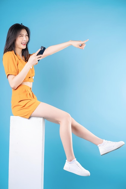 Full length photo of young Asian woman using smartphone on blue background