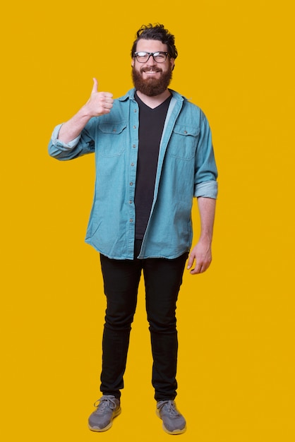 Full length photo of young bearded man standing over yellow