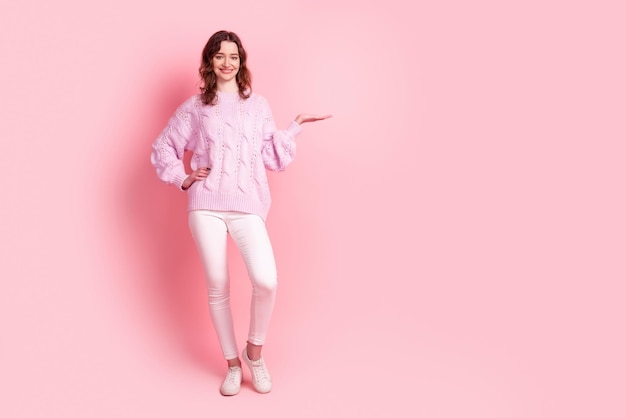 Full length photo of young cheerful woman hold hand promotion offer advertise isolated over pink color background.