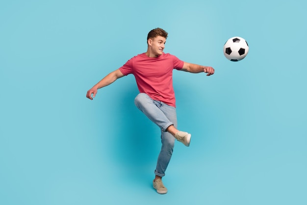 Full length photo of young man play soccer kick ball hobby sportive isolated over blue color background