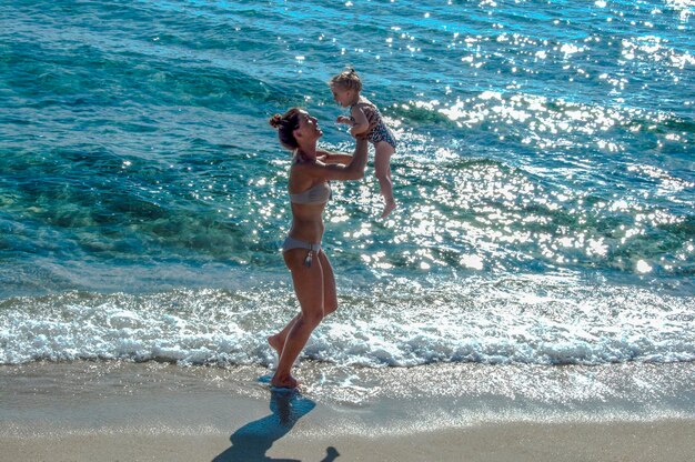 Full length of playful mother lifting daughter while standing on shore at beach during summer