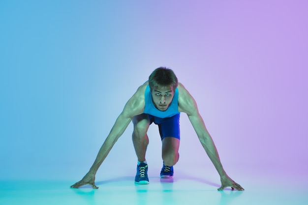 Full length portrait of active young caucasian running, jogging man on background in neon