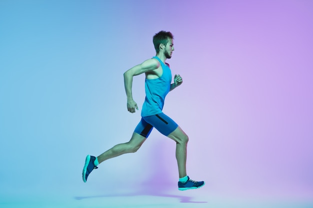 Full length portrait of active young caucasian running, jogging man on neon wall