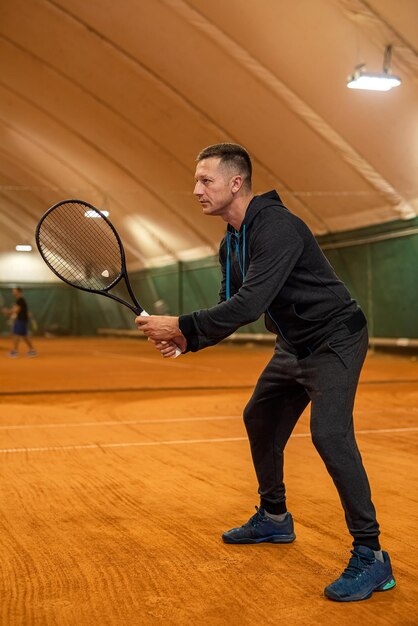 Full length portrait of agile male athlete playing tennis on indoor court