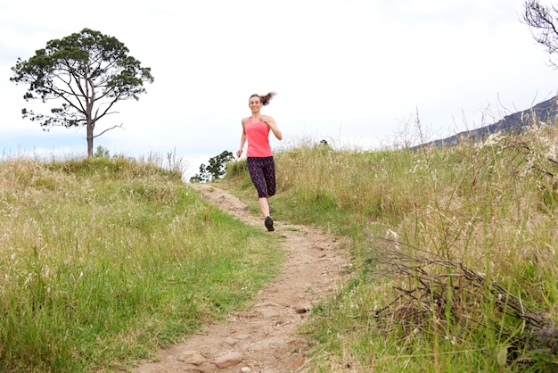 Full length portrait of athletic woman running on dirt path