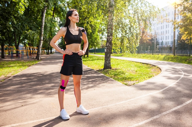 Full length portrait of attractive muscular brunette woman wearing black sports outfit posing outdoors.