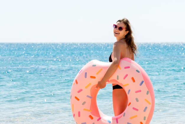 Full length portrait of attractive woman holding doughnut inflatable ring on the beach at the sea background Have happy summer