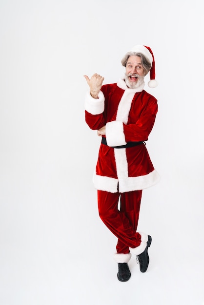 Full length Portrait of bearded gray-haired Santa Claus man in red costume pointing finger aside isolated on white