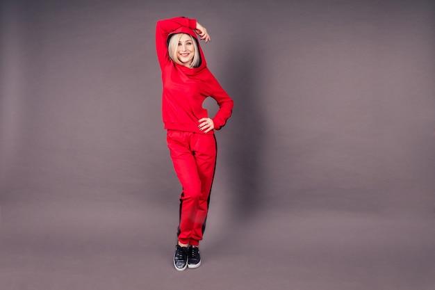 Full-length portrait of a beautiful makeup blonde woman slim in red sports suit posing and stretching in the studio on a black background,hip hop dancer dancing happy model fitness aerobics trainer