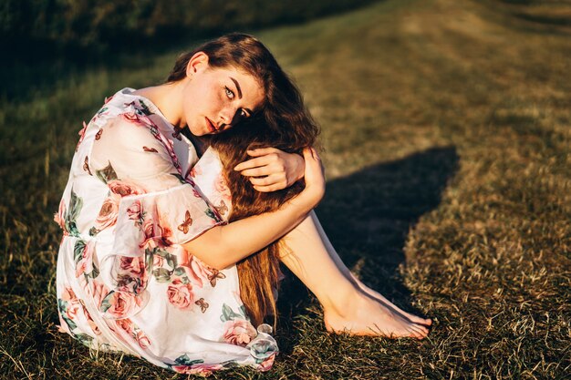 Full length portrait of beautiful woman with long curly hair on
currant field. woman in a light dress sits on the grass in sunny
day