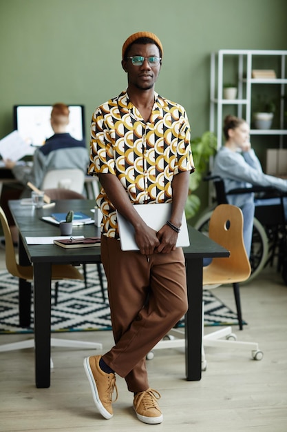 Full length portrait of black young man wearing bright yellow pattern and looking at camera while st