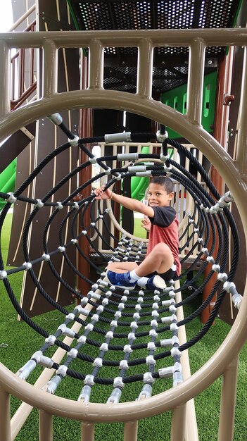 Photo full length portrait of boy sitting in jungle gym at playground