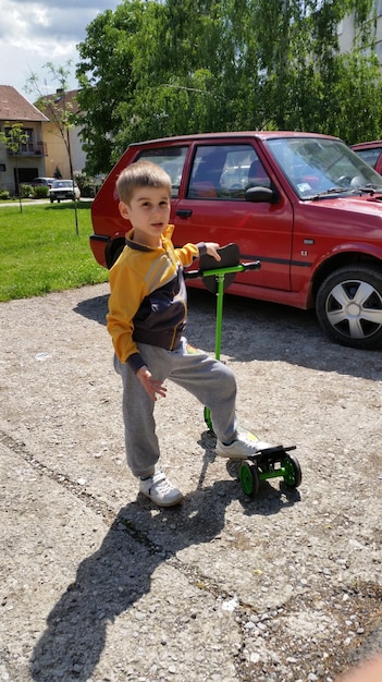 Full length portrait of boy standing with push scooter by car