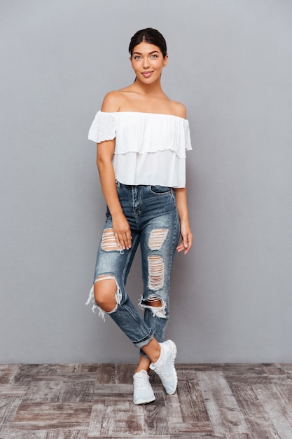 Full length portrait of a casual beautiful woman posing isolated on a gray wall