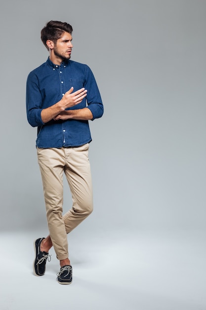 Full length portrait of a casual man standing with legs crossed over gray wall