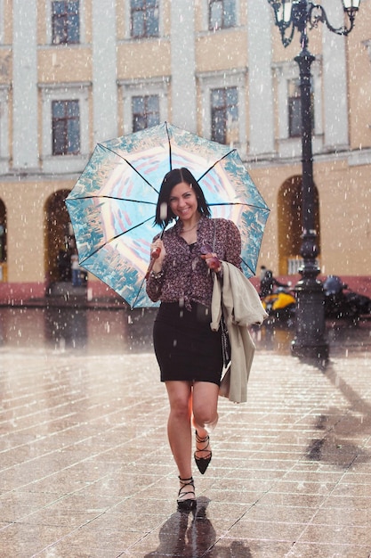full length portrait of cheerful woman walking with umbrella at fountain
