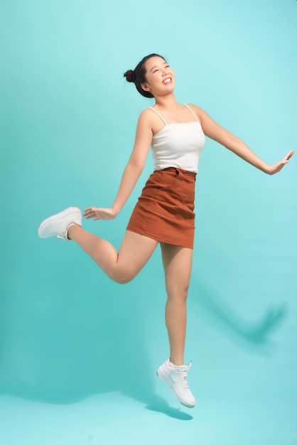 Full length portrait of a cheerful young woman jumping and celebrating over blue background