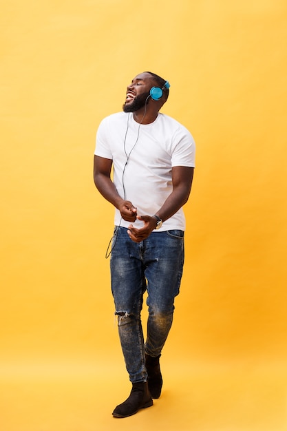 Full length portrait of a cherry young african american man listening to music with headphones and dancing  