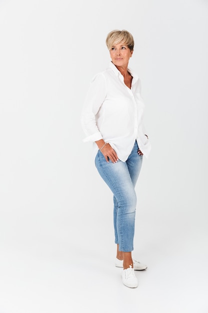 Full length portrait closeup of mature woman with short blond hair looking at camera isolated over white wall in studio