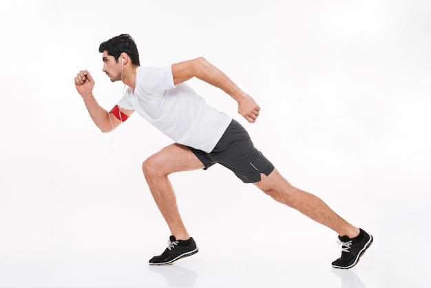 Full length portrait of a concentrated young sports man running with earphones isolated on a white background