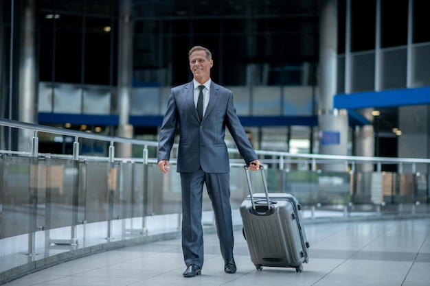 Full-length portrait of a contented businessman trundling his\
trolley suitcase by the telescopic metal handle