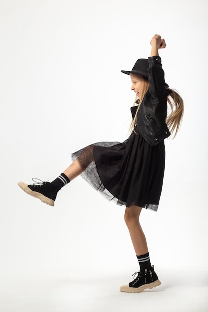 Портрет танцующей молодой девушки с длинными каштановыми волосами, одетой в хулиганском стиле, в полный рост.
