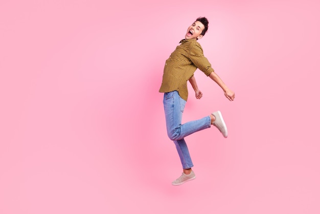 Full length portrait of excited young man in shirt jumping isolated over pastel color background