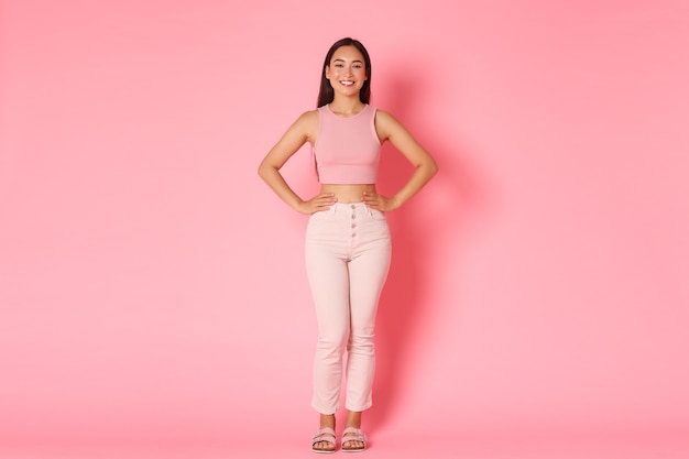 Full length portrait of fashionable brunette asian girl standing over pink