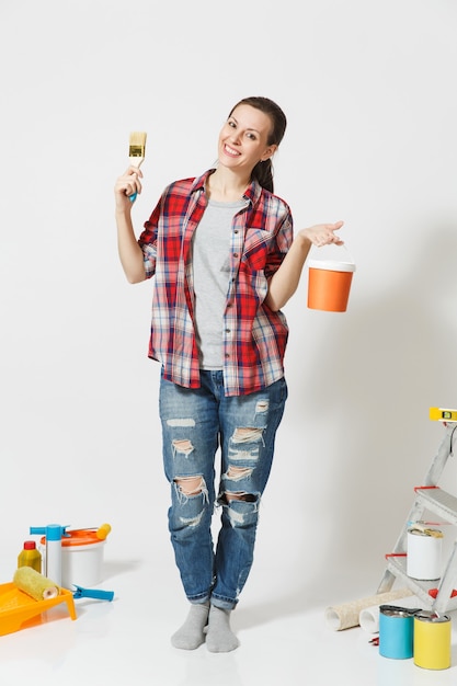 Full length portrait of fun cute woman with brush, paint can standing near instruments for renovation apartment home isolated on white background. Wallpaper, gluing accessories, tools. Repair concept.