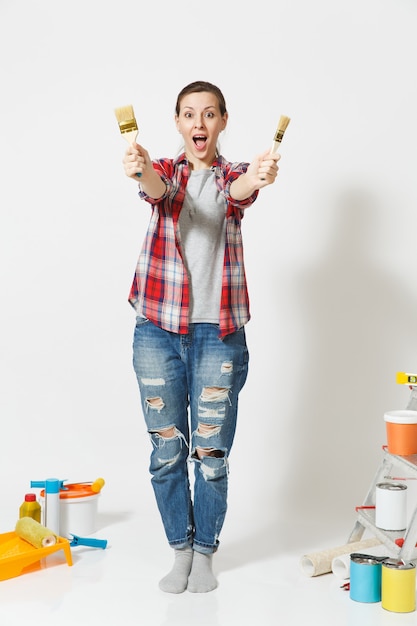 Full length portrait of fun cute woman with brush standing near instruments for renovation apartment home isolated on white background. Wallpaper accessories for gluing painting tools. Repair concept.