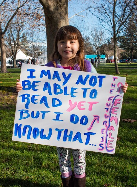 Photo full length portrait of girl holding text in paper while standing on field