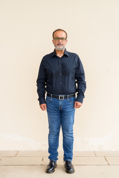 Full length portrait of handsome bearded Indian man against plain wall