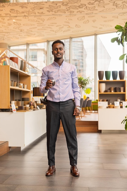 Full length portrait of handsome black businessman indoors at coffee shop