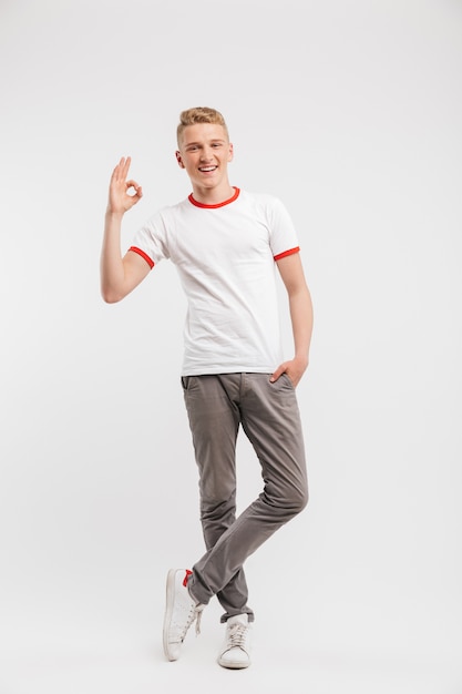 Full length portrait of handsome hipster boy wearing casual clothing smiling and showing ok sign to you, isolated over white