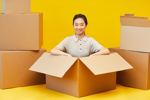 Full length portrait of happy Asian woman sitting in box and looking
