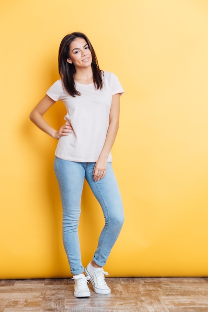 Full length portrait of a happy casual woman standing on yellow wall