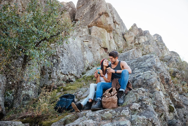 Full length portrait of a happy couple resting while hiking in mountains