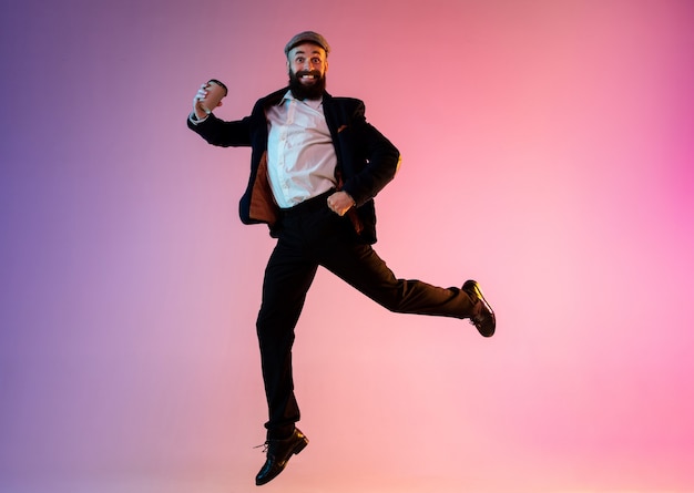 Full length portrait of happy jumping man in neon light and gradient background